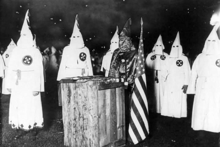 Decoration only: An old, black-and-white photo depicting several hooded members of the KKK at a Klan rally.