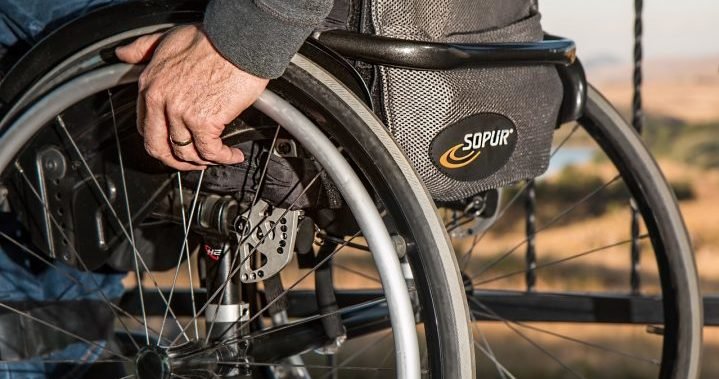 Decoration only: A photo of a person sitting in a wheelchair with a hand on one of the wheels. The photo is cropped so you can only see the lower half of the person from the stomach down.