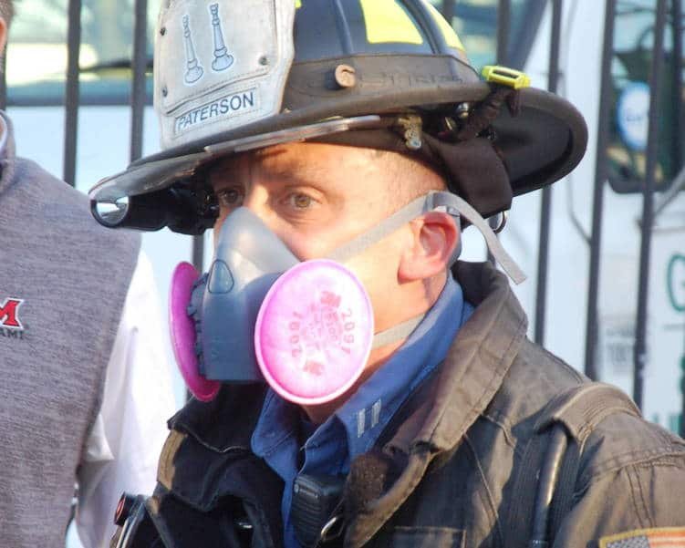 A Paterson firefighter wearing a mask and helmet looks off to the side.