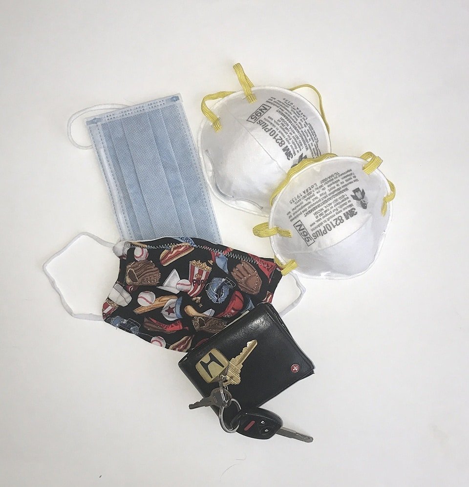 A wallet and keys on a table among a pile of facemasks.