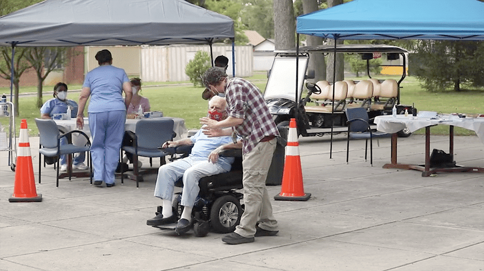 A man stands and speaks to another man in a wheelchair.