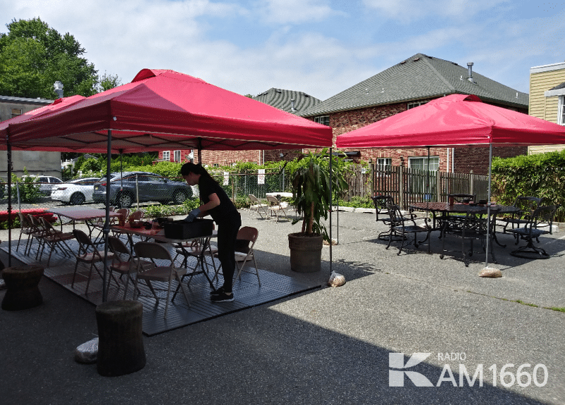 A restaurant server setting a table underneath red canvas overhead tents.