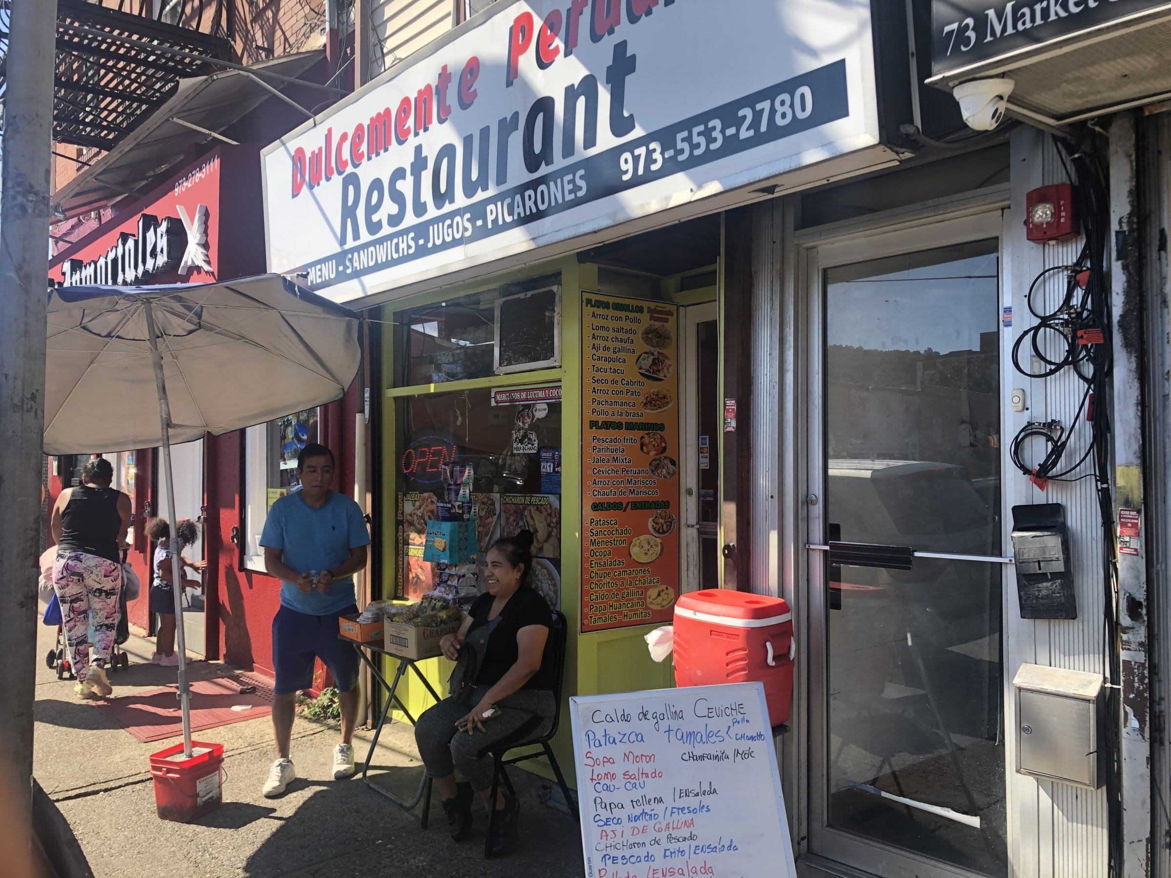 Two people sit on the sidewalk outside of a New Jersey restaurant.