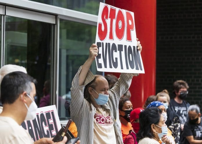 A man at a protest wearing a facemask holds a sign that reads, "STOP EVICTION."