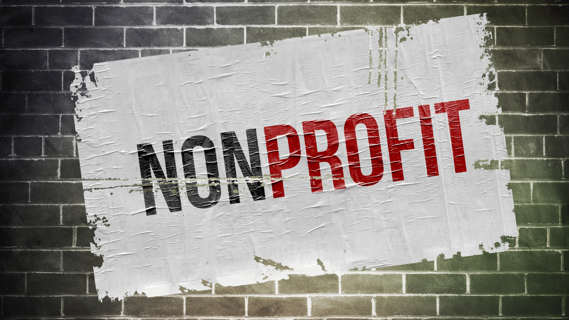 A white piece of paper has been slapped onto a brick wall at a slight diagonal slant, with the word "NONPROFIT" written in bold, all-caps across the paper.