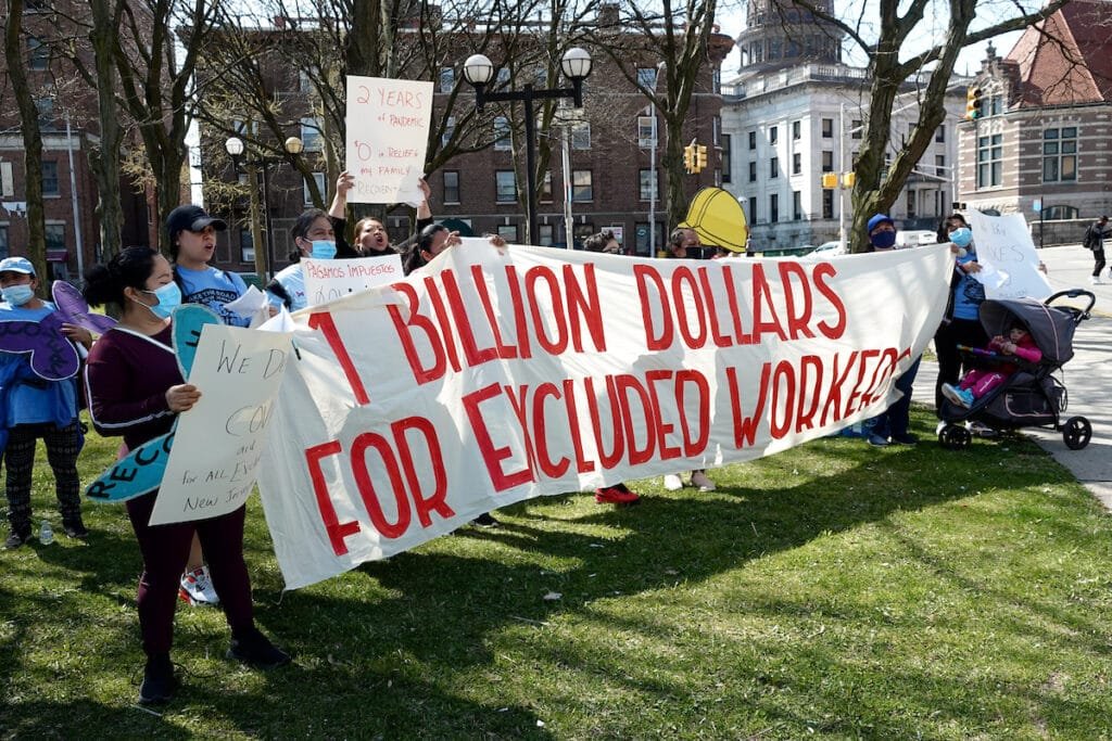 A group of demonstrators holds up a banner that reads "1 billion dollars for excluded workers."